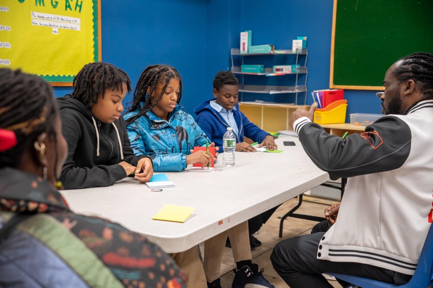 A facilitator guides middle school students through a hands-on writing activity at a classroom table.