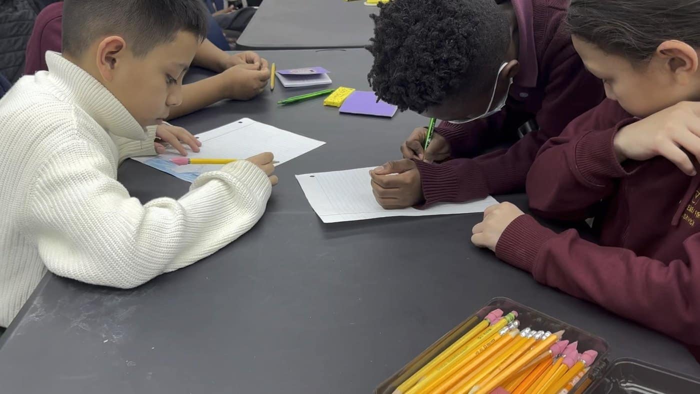 Students take part in a reflection activity while seated in a school gym.